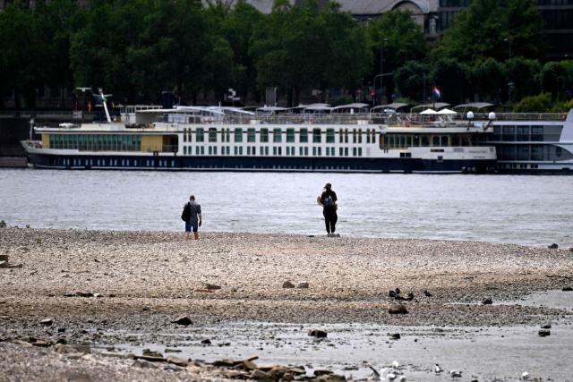 People walk next to the partially dried-up river bed at the Rhine in Cologne, western Germany, on July 6, 2026, following exceptionally hot weather. (Photo by Ina FASSBENDER / AFP)