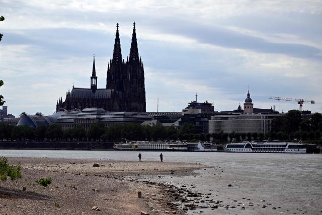 People walk next to the partially dried-up river bed with the Cologne cathedral in the background at the Rhine in Cologne, western Germany, on July 6, 2026, following exceptionally hot weather. (Photo by Ina FASSBENDER / AFP)