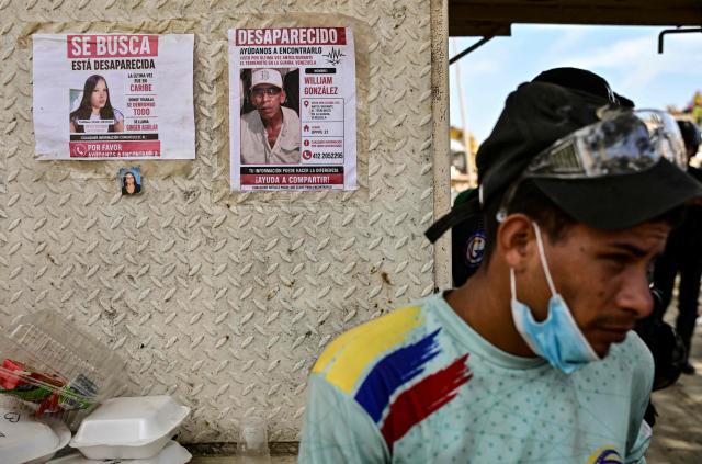 Posters of missing people are displayed on a wall as a resident stands nearby in the Caribe sector of Caraballeda, La Guaira state, Venezuela, on July 6, 2026, following powerful earthquakes that struck the region. The earthquakes that struck Venezuela on June 24 have claimed the lives of at least 3,342 people, the Venezuelan government reported on July 5. (Photo by MARTIN BERNETTI / AFP)