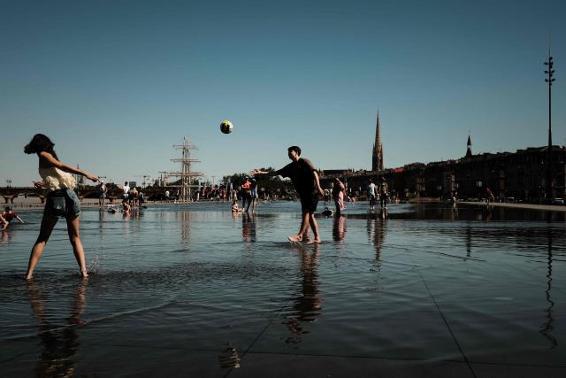 A man plays with a ball as he cools off in the Miroir d'eau reflecting pool on the banks of the Garonne river, during a summer heatwave in Bordeaux, south-western France, on July 6, 2026. For the third time in six weeks, France is facing a surge in temperatures, with three-quarters of the country under a heatwave alert on July 7, 2026, just a few days after a historic heatwave. (Photo by Philippe LOPEZ / AFP)