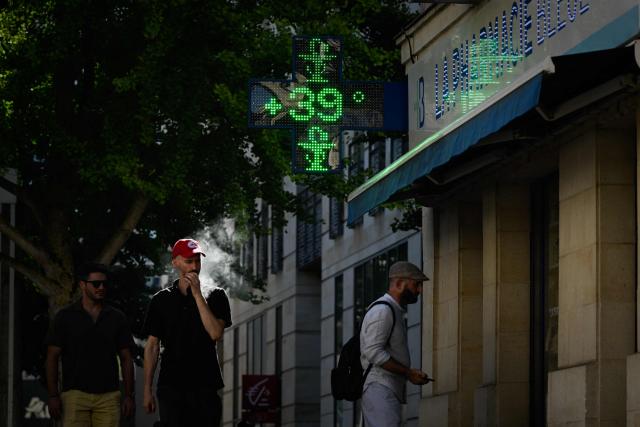 Pedestrians walk past the illuminated green cross of a pharmacy reading "39 degrees Celsius" in Bordeaux, south-western France, on July 6, 2026. For the third time in six weeks, France is facing a surge in temperatures, with three-quarters of the country under a heatwave alert on July 7, 2026, just a few days after a historic heatwave. (Photo by Philippe LOPEZ / AFP)