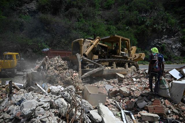 A man searches for recyclable materials among debris as heavy machinery clears rubble from collapsed buildings in Caraballeda, La Guaira state, Venezuela, on July 6, 2026, following powerful earthquakes that struck the region. The earthquakes that struck Venezuela on June 24 have claimed the lives of at least 3,342 people, the Venezuelan government reported on July 5. (Photo by Federico PARRA / AFP)