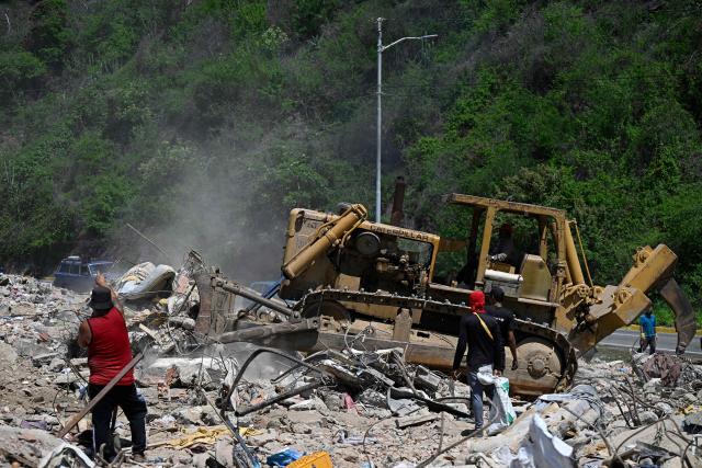 People search for recyclable materials among debris as heavy machinery clears rubble from collapsed buildings in Caraballeda, La Guaira state, Venezuela, on July 6, 2026, following powerful earthquakes that struck the region. The earthquakes that struck Venezuela on June 24 have claimed the lives of at least 3,342 people, the Venezuelan government reported on July 5. (Photo by Federico PARRA / AFP)