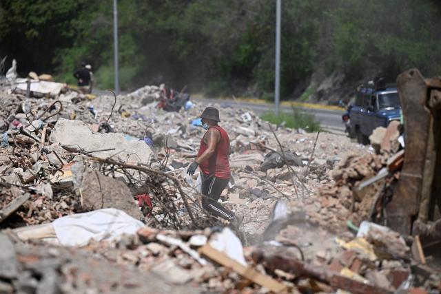 A man searches for recyclable materials among debris as heavy machinery clears rubble from collapsed buildings in Caraballeda, La Guaira state, Venezuela, on July 6, 2026, following powerful earthquakes that struck the region. The earthquakes that struck Venezuela on June 24 have claimed the lives of at least 3,342 people, the Venezuelan government reported on July 5. (Photo by Federico PARRA / AFP)