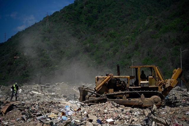 A man searches for recyclable materials among debris as heavy machinery clears rubble from collapsed buildings in Caraballeda, La Guaira state, Venezuela, on July 6, 2026, following powerful earthquakes that struck the region. The earthquakes that struck Venezuela on June 24 have claimed the lives of at least 3,342 people, the Venezuelan government reported on July 5. (Photo by Federico PARRA / AFP)