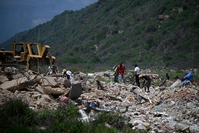 People search for recyclable materials among debris as heavy machinery clears rubble from collapsed buildings in Caraballeda, La Guaira state, Venezuela, on July 6, 2026, following powerful earthquakes that struck the region. The earthquakes that struck Venezuela on June 24 have claimed the lives of at least 3,342 people, the Venezuelan government reported on July 5. (Photo by Federico PARRA / AFP)