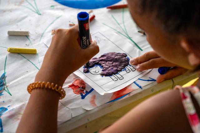 A child displaced by the June 24 earthquake works on a craft using coloured clay at a temporary shelter set up at the Jose Maria Vargas sports complex in Catia la Mar, La Guaira state, Venezuela, on July 6, 2026. The twin earthquakes that struck Venezuela on June 24 have claimed the lives of at least 3,535 people, the Venezuelan government reported on July 5. (Photo by Miguel MEDINA / AFP)