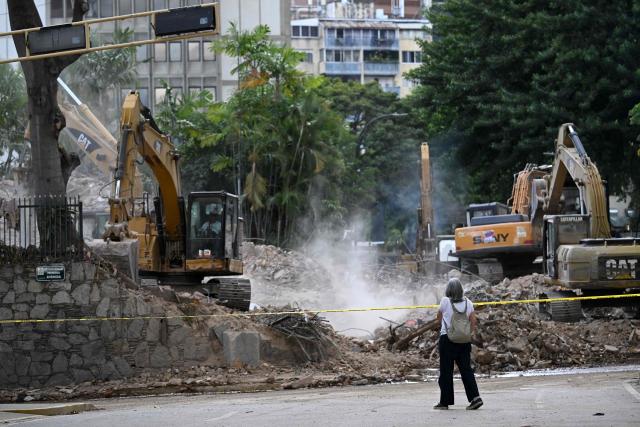 A local stares at heavy machinery removing debris form a collapsed building at the Chacao municipality in Caracas, on July 6, 2026, following the June 24 earthquakes that hit the region. The death toll from Venezuela's twin earthquakes has risen to 3,535, with more than 16,700 injured in the disaster, according to updated official figures released on July 6. (Photo by Raul ARBOLEDA / AFP)