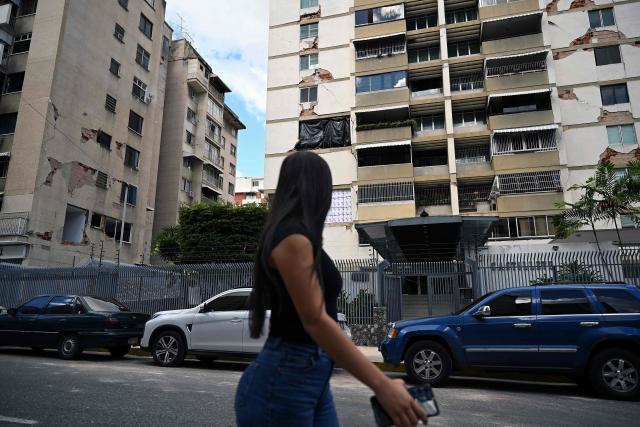 A woman walks past damaged buildings which will undergo official inspection to determine their habitability in Caracas, on July 6, 2026, following the June 24 earthquakes that hit the region. The death toll from Venezuela's twin earthquakes has risen to 3,535, with more than 16,700 injured in the disaster, according to updated official figures released on July 6. (Photo by Raul ARBOLEDA / AFP)