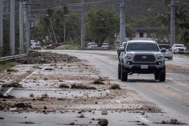 A motorist drives past debris scattered across a road after strong winds and heavy rain brought by Typhoon Bavi in Guam on July 7, 2026. (Photo by Yuichi YAMAZAKI / AFP)
