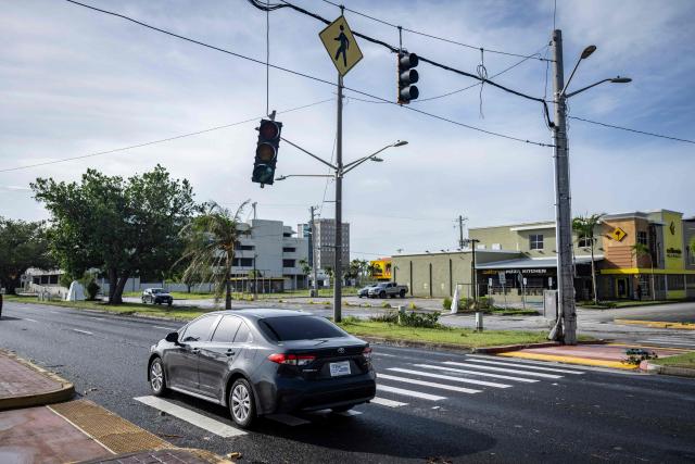 A traffic signal hangs from its support after being dislodged by strong winds brought by Typhoon Bavi in Guam on July 7, 2026. (Photo by Yuichi YAMAZAKI / AFP)
