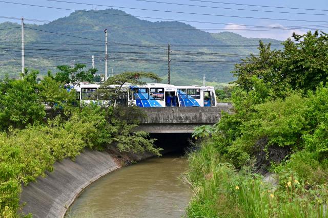 Buses travel across a vehicular bridge spanning what is popularly known as the Canal de la Muerte (Death Canal), in northwest Guayaquil, Ecuador, on June 29, 2026. Hundreds of bodies linked to kidnapping victims, criminal acts, and clashes between gangs have been found at he Canal de la Muerte -a section of the Daule–Santa Elena transfer canal. (Photo by MARCOS PIN / AFP)