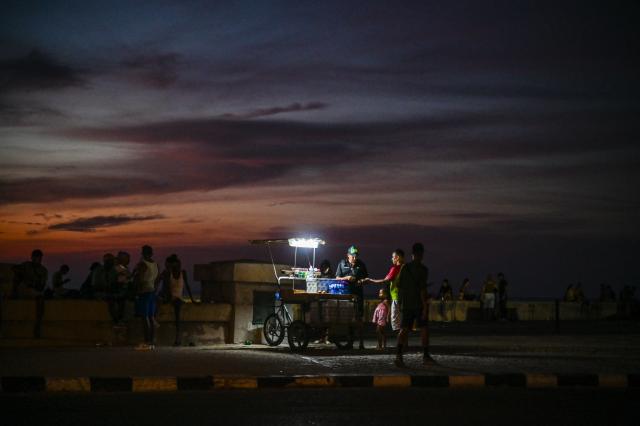 A street vendor uses a portable lamp to sell goods along the Malecon during a nationwide blackout in Havana on July 6, 2026. Cuba on July 6 suffered its third nationwide power outage since the start of the year, the state electricity company said. The impoverished island was already struggling to keep the lights on before US President Donald Trump in January imposed an oil blockade, which has depleted the already dwindling supply of fuel for Cuba's power plants. (Photo by ADALBERTO ROQUE / AFP)