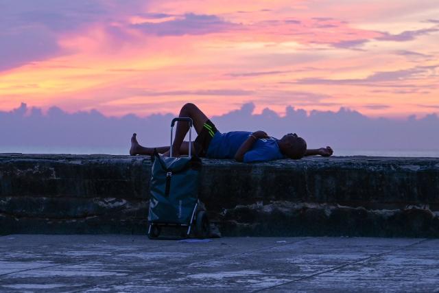 A person lies on the Malecon at sunset during a nationwide blackout in Havana on July 6, 2026. Cuba on July 6 suffered its third nationwide power outage since the start of the year, the state electricity company said. The impoverished island was already struggling to keep the lights on before US President Donald Trump in January imposed an oil blockade, which has depleted the already dwindling supply of fuel for Cuba's power plants. (Photo by ADALBERTO ROQUE / AFP)