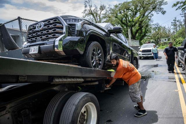 A worker loads a vehicle disabled by flooding caused by Super Typhoon Bavi onto a car carrier in Guam on July 7, 2026. (Photo by Yuichi YAMAZAKI / AFP)