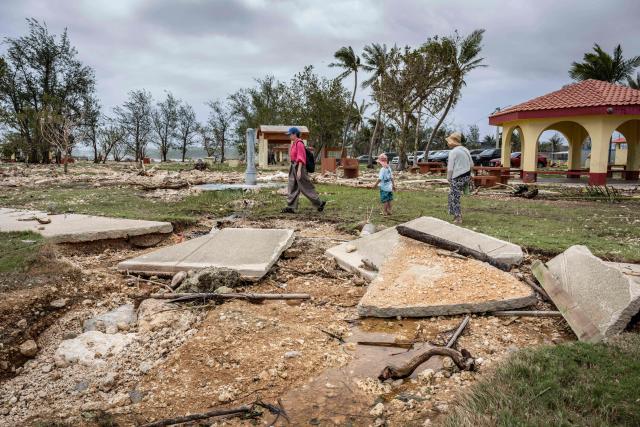 People walk past a damaged walkway at a park in the aftermath of Super Typhoon Bavi in Guam on July 7, 2026. (Photo by Yuichi YAMAZAKI / AFP)