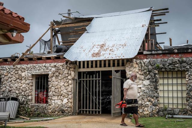 A worker walks out of a maintenance building with a roof damaged by strong winds brought by Super Typhoon Bavi in Guam on July 7, 2026. (Photo by Yuichi YAMAZAKI / AFP)