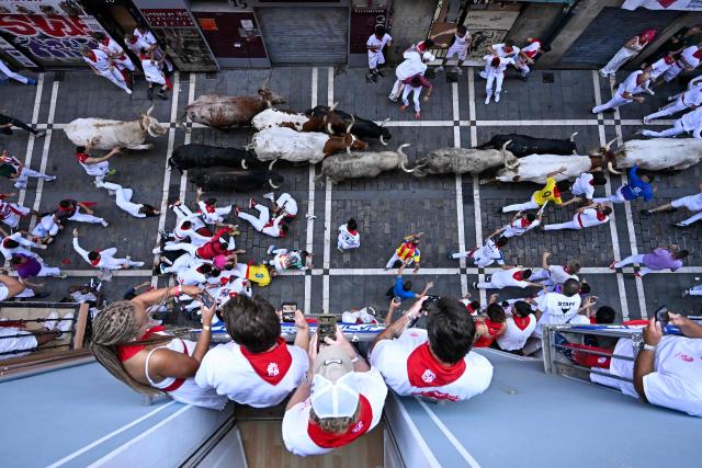 People watch from a balcony as participants run ahead of bulls from the Fuente Ymbro bull ranch during the first running of the bulls of the San Fermin festival in Pamplona, northern Spain, on July 7, 2026. Thousands of people every year attend the week-long festival and its famous 'encierros', or running of the bulls, in which six bulls are released at 8:00 a.m. evey day to run from their corral to the bullring through the narrow streets of the old town over an 850 meters (yards) course while runners ahead of them try to stay close to the bulls without falling over or being gored. (Photo by ANDER GILLENEA / AFP)