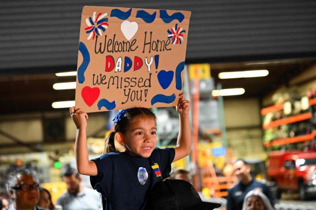 A child holds a sign for her dad as busses arrive with the Los Angeles County Fire Department USA-2 international urban search and rescue team to reunite them with their families after returning from rescue efforts following the earthquakes in Venezuela at the LACoFD Technical Operations Section in Los Angeles, California on July 6, 2026. (Photo by Patrick T. Fallon / AFP)