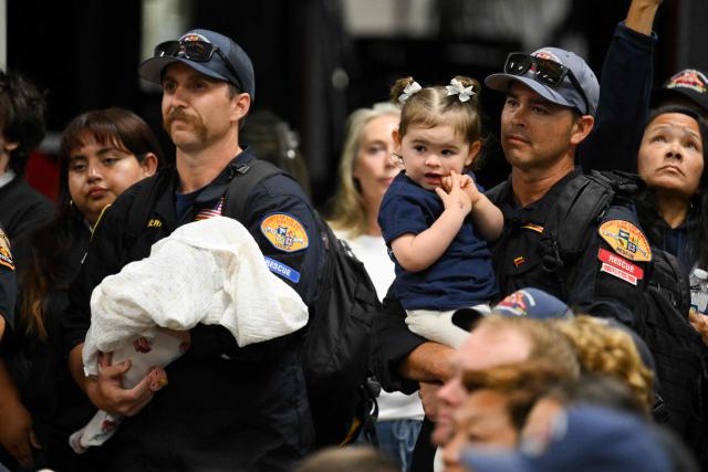 Members of the Los Angeles County Fire Department USA-2 international urban search and rescue team hold their children after reuniting with their families upon returning from rescue efforts following the earthquakes in Venezuela at the LACoFD Technical Operations Section in Los Angeles, California on July 6, 2026. (Photo by Patrick T. Fallon / AFP)