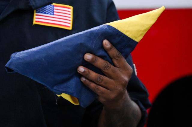 Assistant Fire Chief Trey Espy, USA-2 Task Force Leader, holds a Venezuelan flag while speaking to members of the Los Angeles County Fire Department USA-2 international urban search and rescue team after returning from rescue efforts following the earthquakes in Venezuela, at the LACoFD Technical Operations Section in Los Angeles, California on July 6, 2026. (Photo by Patrick T. Fallon / AFP)