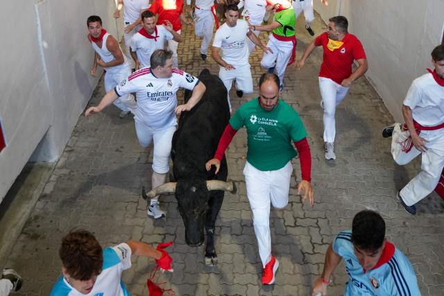 Participants run next to a bull from the Fuente Ymbro bull ranch in a tunnel leading to the bullring during the first running of the bulls of the San Fermin festival in Pamplona, northern Spain, on July 7, 2026. Thousands of people every year attend the week-long festival and its famous 'encierros', or running of the bulls, in which six bulls are released at 8:00 a.m. evey day to run from their corral to the bullring through the narrow streets of the old town over an 850 meters (yards) course while runners ahead of them try to stay close to the bulls without falling over or being gored. (Photo by CESAR MANSO / AFP)