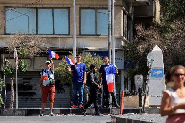 Bystanders wave French national flag in front of France's President's hotel during his visit in Damascus on July 7, 2026. Syria's President Ahmed al-Sharaa hailed France's "constructive role" in the transition since the toppling of longtime ruler Bashar al-Assad, as French leader Emmanuel Macron made the first post-conflict visit to Damascus by a Western European leader. (Photo by Ludovic MARIN / POOL / AFP)