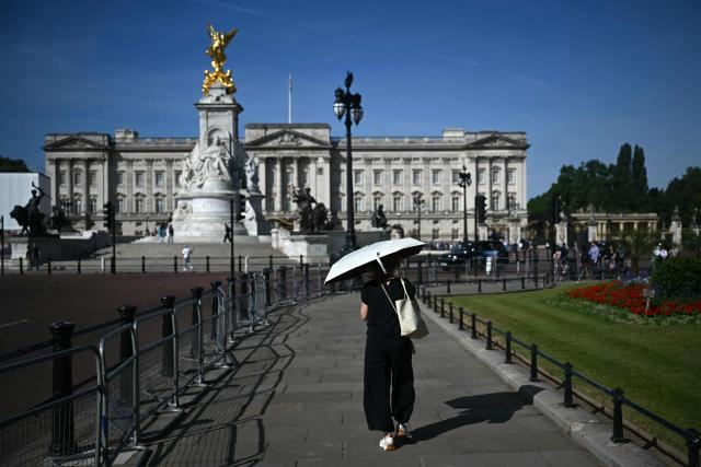 A person uses a parasol umbrella to shelter from the heat of the sun during a heatwave, as they walk near Buckingham Palace, in central London on July 7, 2026. (Photo by JUSTIN TALLIS / AFP)