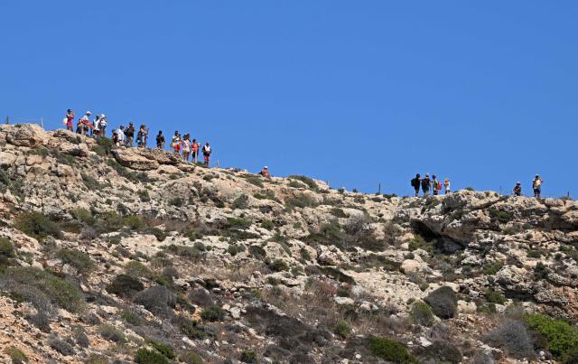 People enjoy the view from the cliffs while walking down to Rabbit Beach in the Italian island of Lampedusa, a protected nature reserve with limited daily visitor access to avoid over tourism, on July 6, 2026. (Photo by Tiziana FABI / AFP)