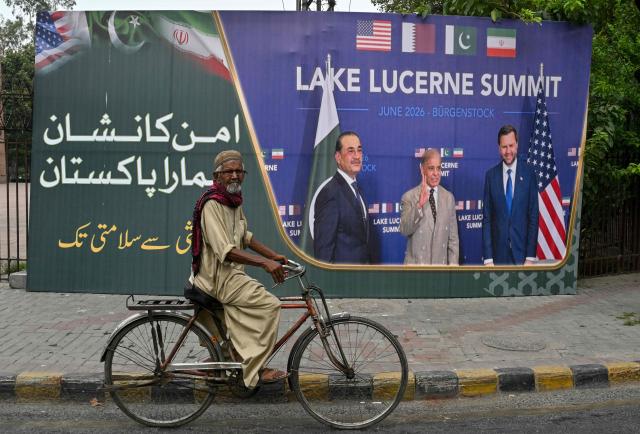 A man cycles past a billboard featuring Pakistan's Prime Minister Shehbaz Sharif, Pakistan's Chief of Army Staff Field Marshal Asim Munir and the US Vice President JD Vance in Lahore on July 7, 2026 during the Lake Lucerne Summit in Switzerland earlier in June. (Photo by Arif ALI / AFP)