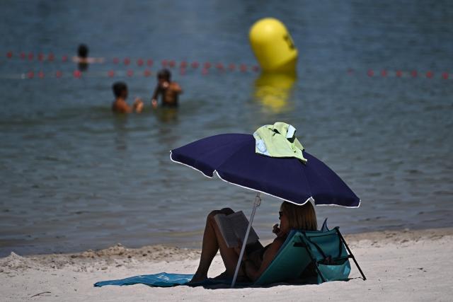 A woman reads a book in the shade of a sun umbrella at the Bègles lake in Bègles, on the outskirts of Bordeaux, south-western France on July 7, 2026, as another heatwave hits France. (Photo by Christophe ARCHAMBAULT / AFP)
