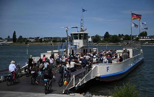 Schoolchildren on bicycles are taking a car ferry to Mondorf near Bonn, western Germany on July 7, 2026. The dilapidated Bonn North Bridge (Friedrich-Ebert-Brücke) on the A565 has been completely closed to all motor traffic since June 2026. The approach bridge on the left bank of the Rhine has sustained extensive damage, will no longer be opened to traffic, and must be demolished and rebuilt. (Photo by Ina FASSBENDER / AFP)