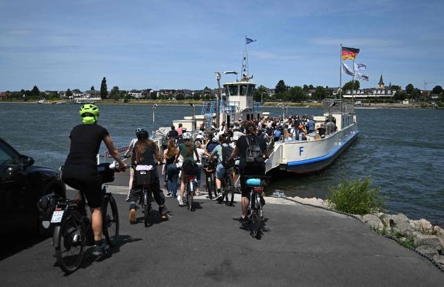 Schoolchildren on bicycles are taking a car ferry to Mondorf near Bonn, western Germany on July 7, 2026. The dilapidated Bonn North Bridge (Friedrich-Ebert-Brücke) on the A565 has been completely closed to all motor traffic since June 2026. The approach bridge on the left bank of the Rhine has sustained extensive damage, will no longer be opened to traffic, and must be demolished and rebuilt. (Photo by Ina FASSBENDER / AFP)