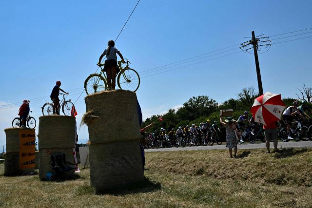 The pack of riders (peloton) cycles past spectators with bicycles atop hay bales at the start of the 5th stage of the 113th edition of the Tour de France cycling race, 158 km between Lannemezan and Pau in southwestern France, on July 8, 2026. (Photo by Jeff PACHOUD / AFP)