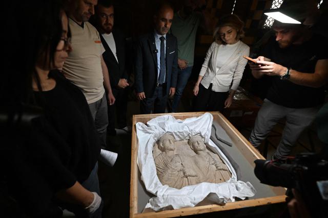 Officials look at a Palmyrene funerary scene dating back to the 2nd–3rd century AD, during the process of the opening the crates of artifacts recovered from France at the National Museum in Damascus on July 8, 2026. The 23 objects returned to the National Museum of Damascus, span a period from prehistory through to the Abbasid era and include artefacts covering the Mesopotamian, Canaanite, Nabataean, Palmyrene, Roman, Byzantine and Umayyad civilisations, according to a statement from the Elysee Palace. (Photo by LOUAI BESHARA / AFP)