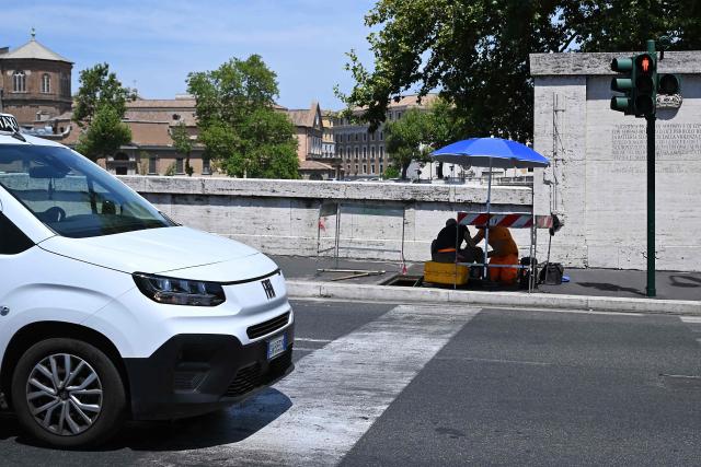 Workers repair telecommunication cables under the sun, protected by umbrellas, at a work site in central Rome on July 8, 2026, as parts of Europe experience another heatwave. (Photo by Andreas SOLARO / AFP)