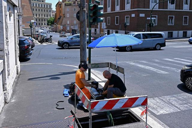 Workers repair telecommunication cables under the sun, protected by umbrellas, at a work site in central Rome on July 8, 2026, as parts of Europe experience another heatwave. (Photo by Andreas SOLARO / AFP)