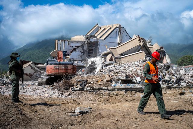 A soldier and a rescue worker are seen next to heavy machinery used in the ruins of a building destroyed by the June 24 earthquakes in Caraballeda, La Guaira state, Venezuela, on July 8, 2026. Venezuela's government called on July 8, 2026 for the release of frozen assets to help raise funds for the country's recovery from last month's twin earthquakes that killed at least 3,600 people. (Photo by Miguel MEDINA / AFP)