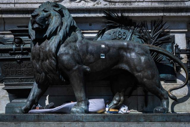 A homeless person lies on a mattress, shielding himself from the sun in the shade of the lion, part of the Statue de la Republique at the Place de la Republique in Paris on July 8, 2026. (Photo by Joel Saget / AFP)
