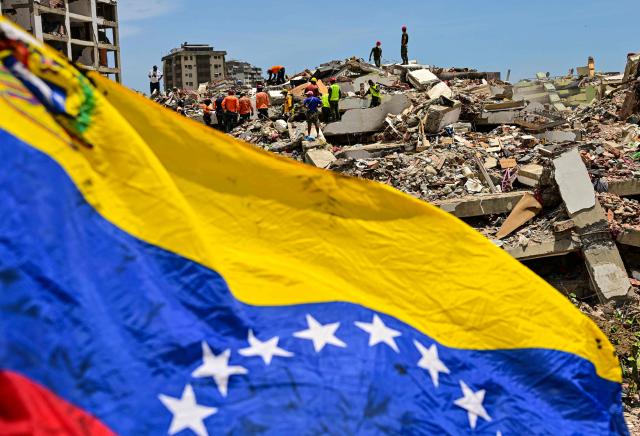 A Venezuelan national flag is seen as rescue workers search for victims in a destroyed building in Caraballeda, La Guaira state, Venezuela, on July 8, 2026, after the June 24 earthquakes. Venezuela's government called on July 8, 2026 for the release of frozen assets to help raise funds for the country's recovery from last month's twin earthquakes that killed at least 3,600 people. (Photo by MARTIN BERNETTI / AFP)