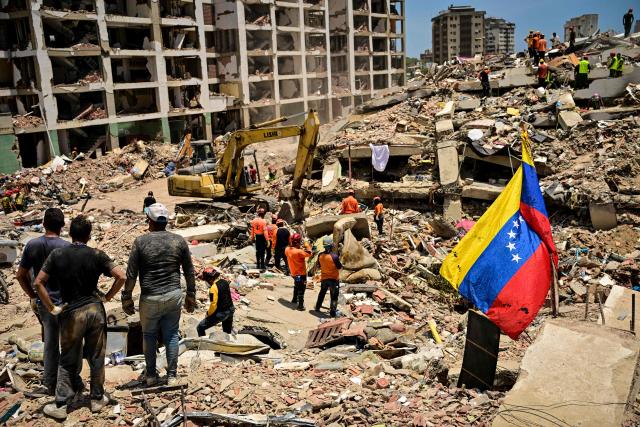 A Venezuelan national flag is seen as rescue workers search for victims in a destroyed building in Caraballeda, La Guaira state, Venezuela, on July 8, 2026, after the June 24 earthquakes. Venezuela's government called on July 8, 2026 for the release of frozen assets to help raise funds for the country's recovery from last month's twin earthquakes that killed at least 3,600 people. (Photo by MARTIN BERNETTI / AFP)