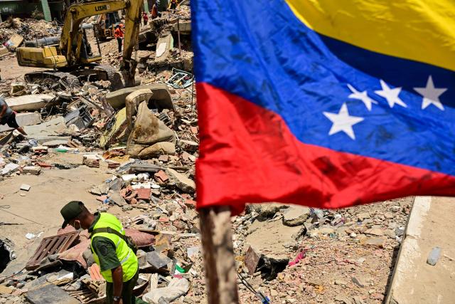 A Venezuelan national flag is seen as rescue workers search for victims in a destroyed building in Caraballeda, La Guaira state, Venezuela, on July 8, 2026, after the June 24 earthquakes. Venezuela's government called on July 8, 2026 for the release of frozen assets to help raise funds for the country's recovery from last month's twin earthquakes that killed at least 3,600 people. (Photo by MARTIN BERNETTI / AFP)