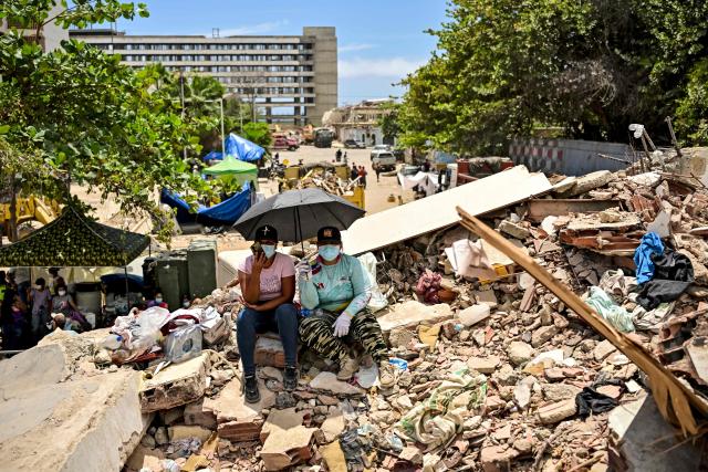 Women wait under an umbrella for the recovery of the corpses of their relatives amid the rubble of a destroyed building in Caraballeda, La Guaira state, Venezuela, on July 8, 2026, after the June 24 earthquakes. Venezuela's government called on July 8, 2026 for the release of frozen assets to help raise funds for the country's recovery from last month's twin earthquakes that killed at least 3,600 people. (Photo by MARTIN BERNETTI / AFP)