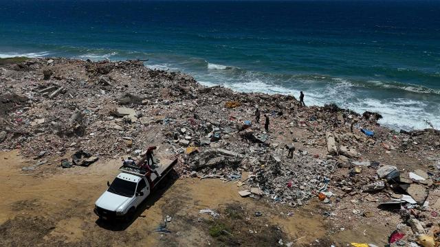 This aerial picture shows people dumping rubble and others searching for scrap metal in the rubble near La Caleta beach in Taraguarena, in the state of La Guaira, Venezuela, on July 8, 2026. Venezuela's government called on July 8, 2026 for the release of frozen assets to help raise funds for the country's recovery from last month's twin earthquakes that killed at least 3,600 people. (Photo by Miguel MEDINA / AFP)