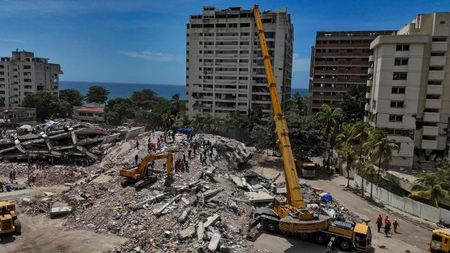 This aerial picture shows heavy machinery, rescuers and volunteers on a destroyed building in Taraguarena, in the state of La Guaira, on July 8, 2026. Venezuela's government called on July 8, 2026 for the release of frozen assets to help raise funds for the country's recovery from last month's twin earthquakes that killed at least 3,600 people. (Photo by Miguel MEDINA / AFP)