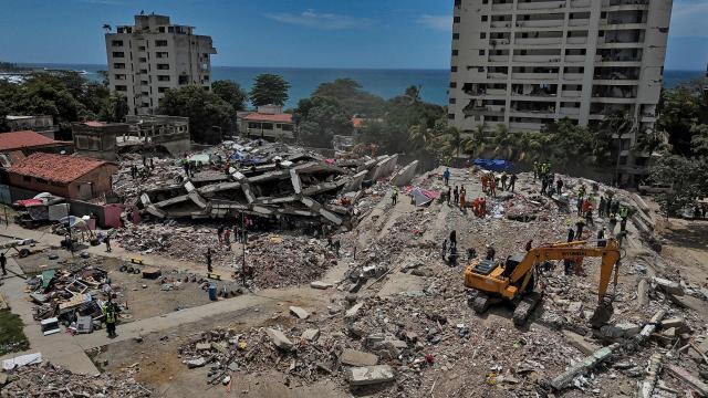 This aerial picture shows heavy machinery, rescuers and volunteers on a destroyed building in Taraguarena, in the state of La Guaira, on July 8, 2026. Venezuela's government called on July 8, 2026 for the release of frozen assets to help raise funds for the country's recovery from last month's twin earthquakes that killed at least 3,600 people. (Photo by Miguel MEDINA / AFP)