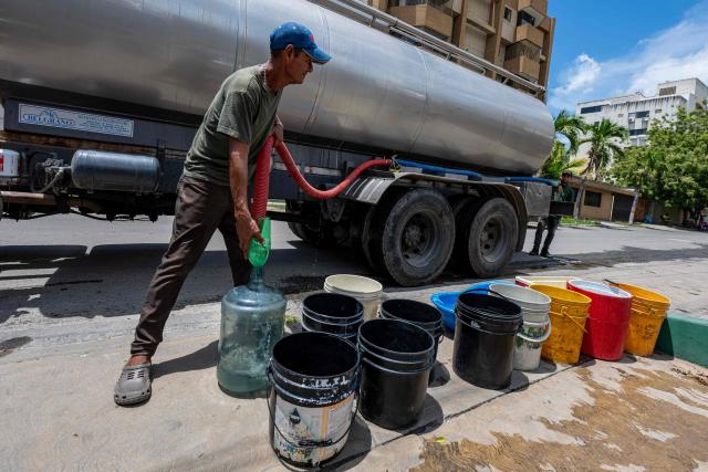 A man distributes water from a water tanker truck in Taraguanena, in the state of La Guaira, Venezuela, on July 8, 2026. Venezuela's government called on July 8, 2026 for the release of frozen assets to help raise funds for the country's recovery from last month's twin earthquakes that killed at least 3,600 people. (Photo by Miguel MEDINA / AFP)