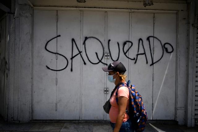 A woman walks past a wall with graffiti reading "Looted"  in Catia La Mar, La Guaira state, Venezuela, on July 8, 2026, following powerful earthquakes that struck the region. Venezuela's government called on July 8, 2026 for the release of frozen assets to help raise funds for the country's recovery from last month's twin earthquakes that killed at least 3,600 people. (Photo by Federico PARRA / AFP)