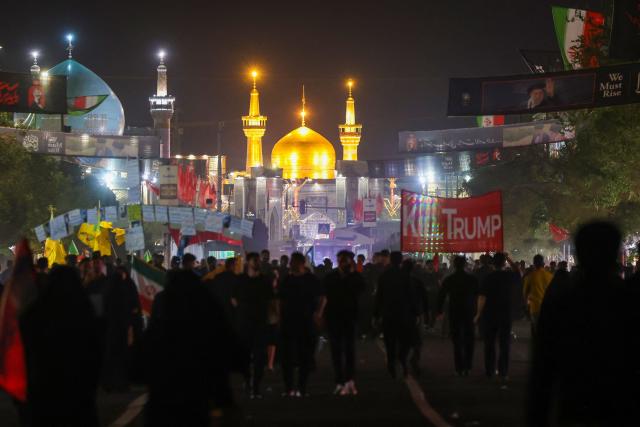TOPSHOT - Mourners walk past an anti-US banner (R) as they arrive to attend the funeral of slain Iranian leader Ali Khamenei and members of his family near Imam Reza's shrine in Mashhad early on July 9, 2026. Iranians were preparing on July 9 to bury their slain leader Ali Khamenei in his hometown of Mashhad in northeast Iran, as new US strikes threatened to trigger a fresh escalation in the Middle East war. The late supreme leader's burial follows a multi-day funeral ceremony that attracted millions of mourners across various cities in both Iran and Iraq. (Photo by ATTA KENARE / AFP) / 