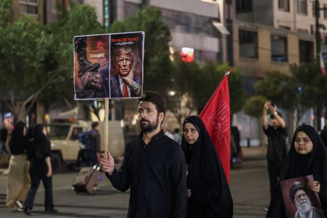 A man holds an anti-US placard as he arrives with others to attend the funeral of slain Iranian leader Ali Khamenei and members of his family near Imam Reza's shrine in Mashhad early on July 9, 2026. Iranians were preparing on July 9 to bury their slain leader Ali Khamenei in his hometown of Mashhad in northeast Iran, as new US strikes threatened to trigger a fresh escalation in the Middle East war. The late supreme leader's burial follows a multi-day funeral ceremony that attracted millions of mourners across various cities in both Iran and Iraq. (Photo by ATTA KENARE / AFP) / 